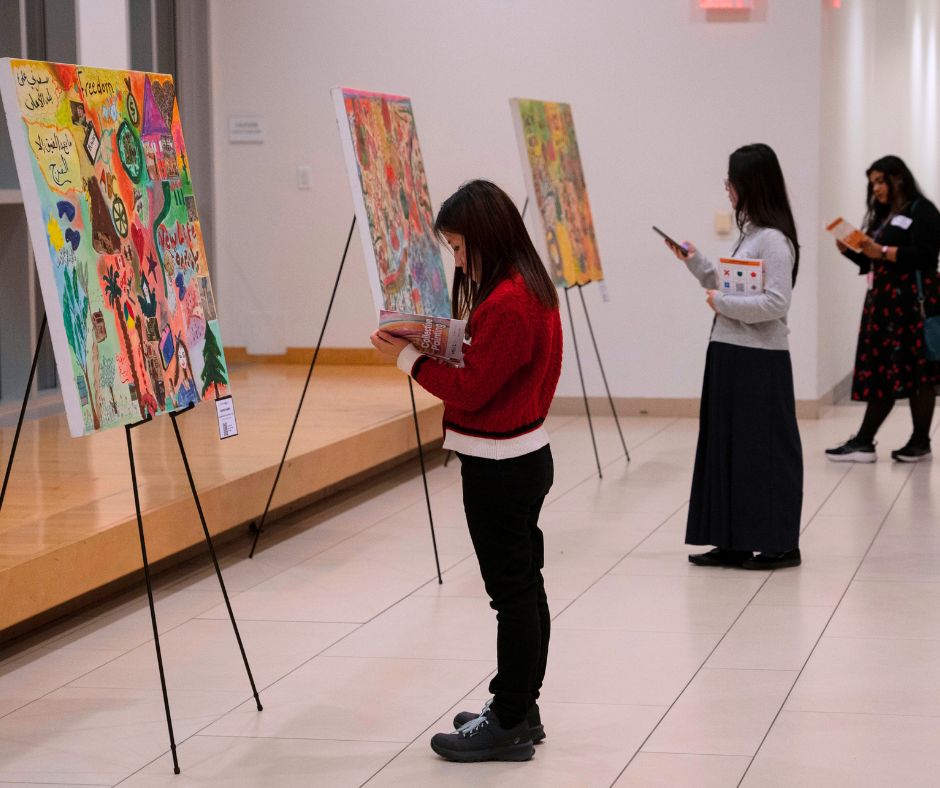 Photo: Healing arts for newcomer family health event on November 12, 2026, attendees observing collective paintings created by HEAL participants.